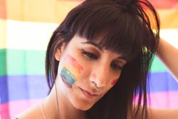 Brunette woman with LGBTQIA symbol on face and eyes down