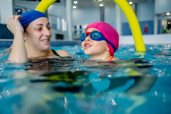 Cheerful girl swimming in pool with mother
