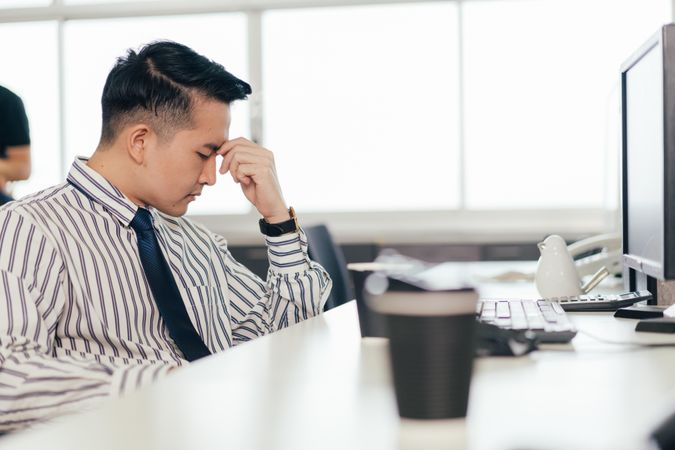 Stressed Asian male employee sitting at desk in the office