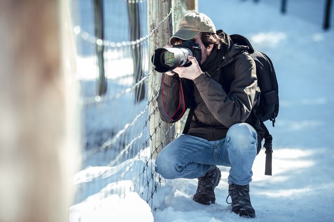 Man taking photo on camera near fence between snow