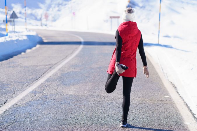 Fit woman in wintry gear stretching quadriceps in the mountains on cold day