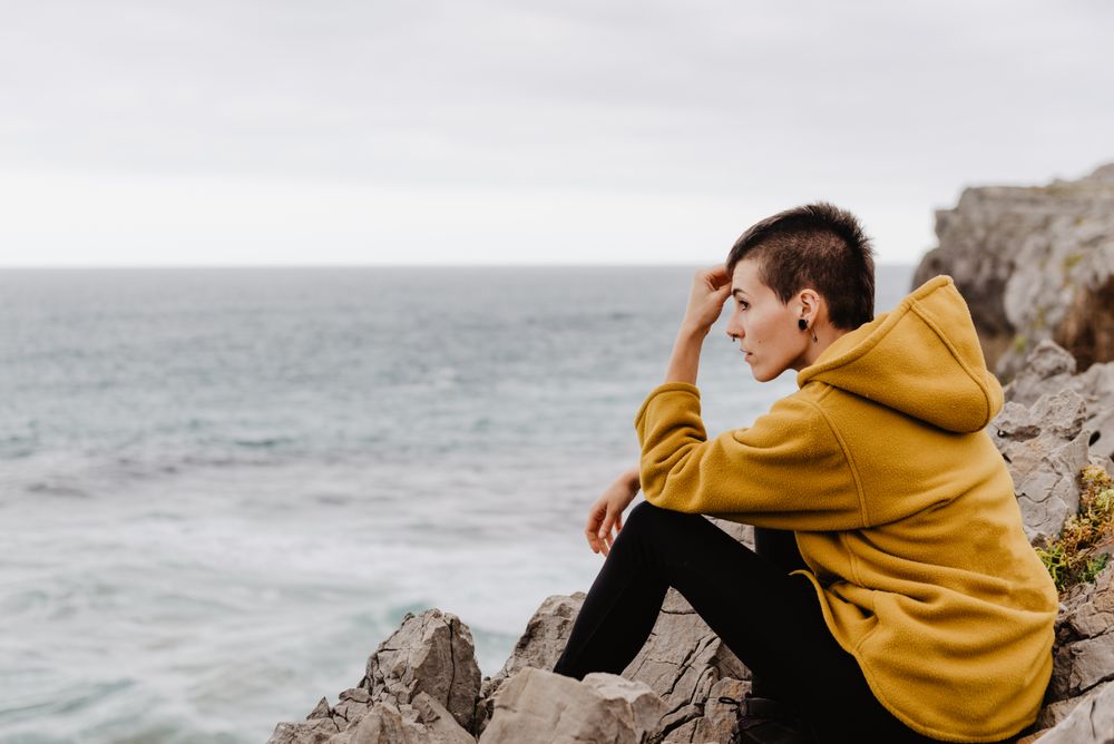 Woman in yellow hoodie on stony shore