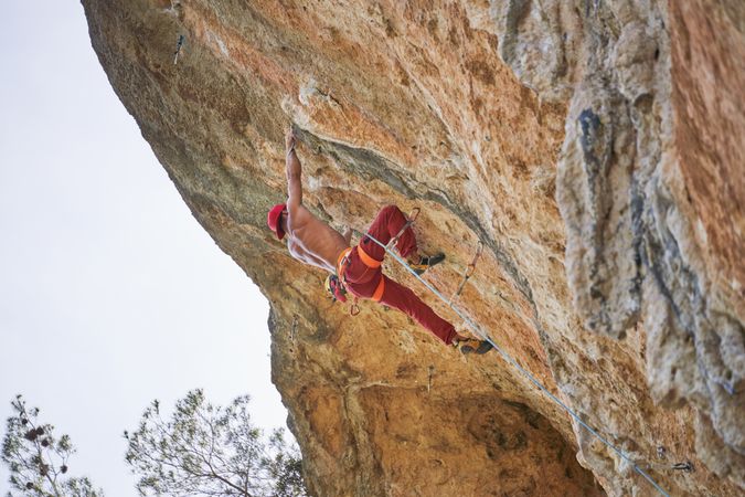 Faceless strong climber holding onto rock while hanging on rope