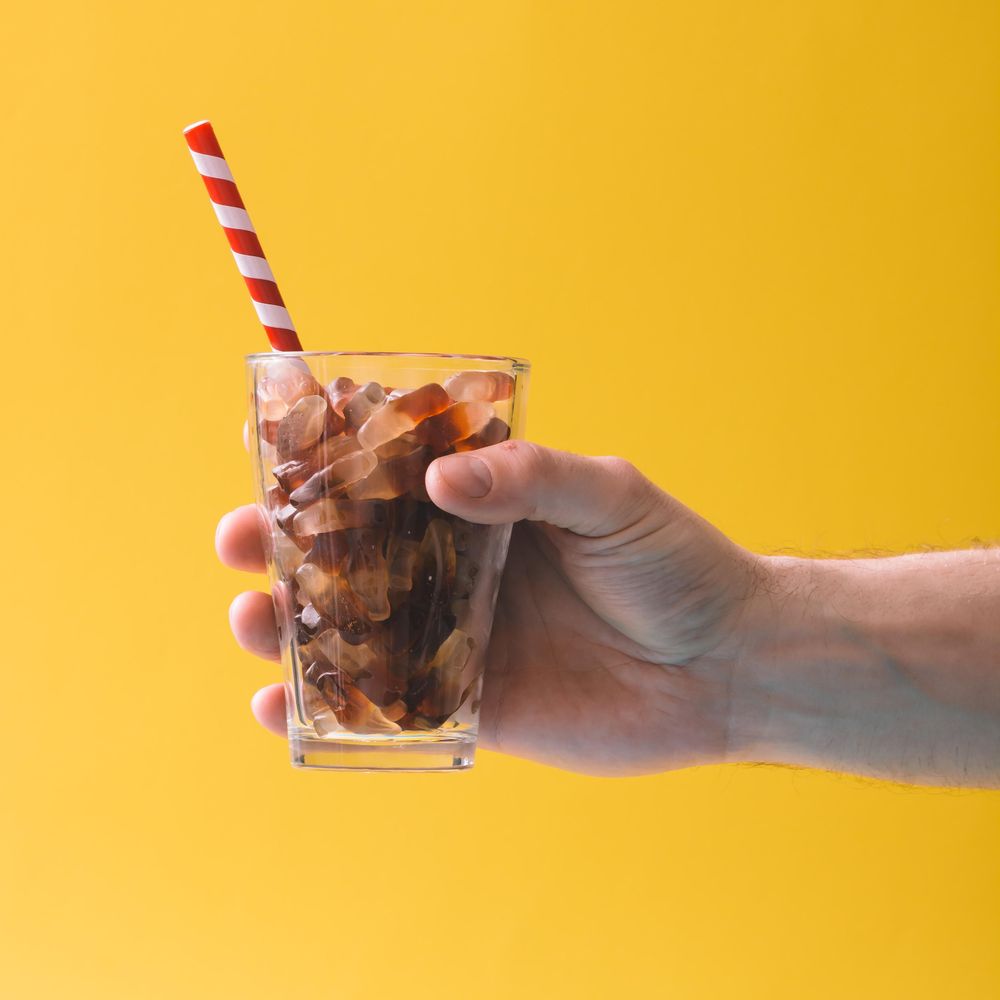 Glass full of gummy candies with straw on yellow background