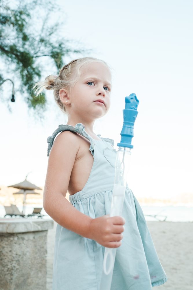 Little girl with bottle of soap bubbles at beach