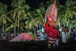 Man performing Theyyam ritual form of dance worship with men at night 0yMoL0