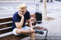 Young Man sitting on a bench with suitcase in the street with his hands on his face worried 5ngZY8