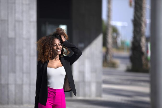 Female in bright pink trousers fixing her hair while strolling outside