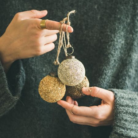 Woman holding three gold Christmas tree decoration, square crop