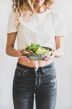 Woman in jeans standing holding vegetarian bowl and green smoothie