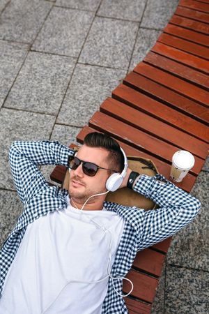 White man with headphones lying on a bench