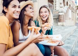 Female friends sitting on steps outside and laughing with pizza