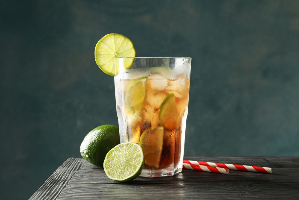Glass of cold cola with citrus and ice on wooden table against dark background