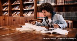 Focused college student studying in library with textbooks on desk 4AWGm0