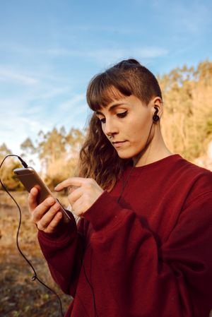 Young woman with piercing listening music on smartphone on hill