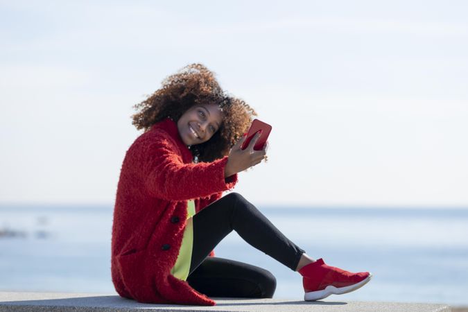Side view of female taking picture on smart phone on bench on the beach