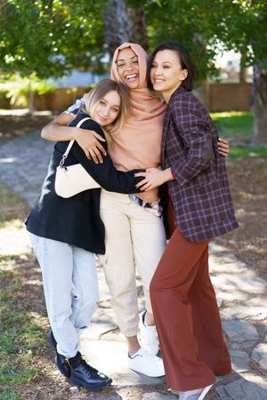 Three women friends standing with their arms around each other in sunny park