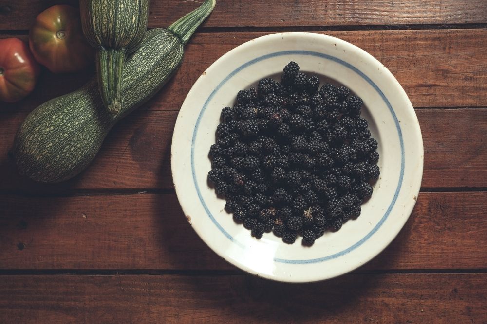 Ripe blackberries garnished by vegetables in bowl on wooden background