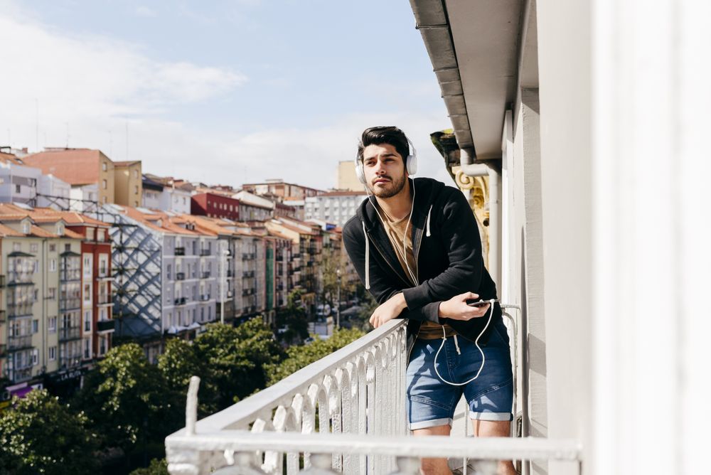 Young happy man holding smartphone on balcony