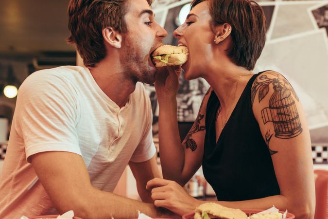 Couple dining at a restaurant biting a burger together
