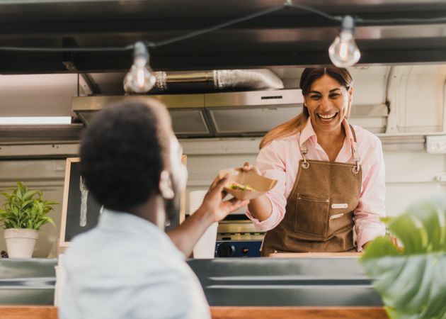 Happy Hispanic seller giving takeaway salad to black client