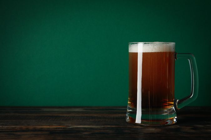 Glass of beer on wooden table against green background