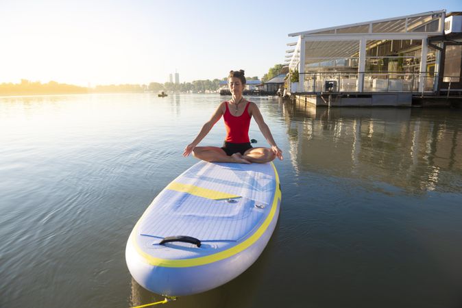 Woman meditating on paddleboard in lake near pier