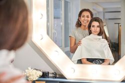Smiling female hairstylist working near mirror with client