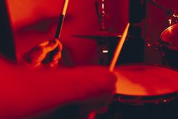 Anonymous man with drumsticks playing on drums in redness