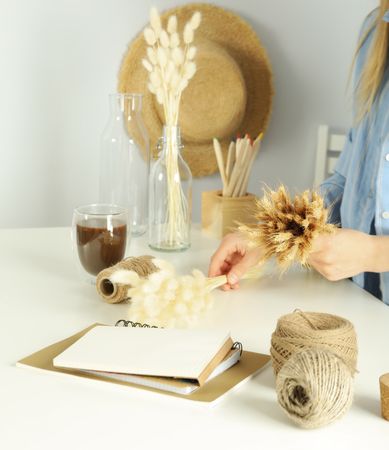 Female in blue striped shirt crafting a dried floral arrangement, square