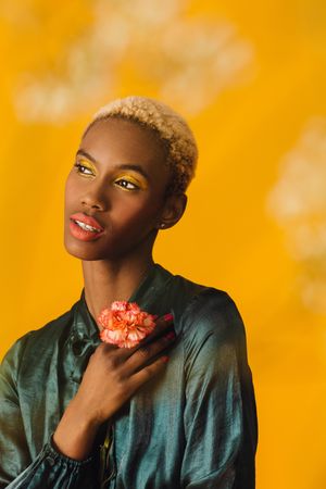 Black woman with short blonde hair holding single carnations to her chest