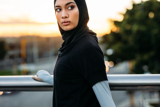 Woman in hijab standing by railing on the road outdoors and looking away