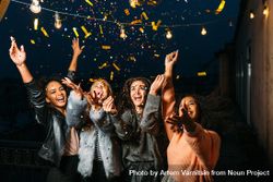 Group of multi-ethnic female friends throwing confetti at night 4M8p15