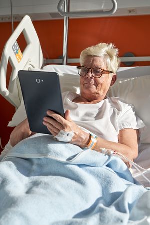 Older female patient using tablet lying on couch in clinic