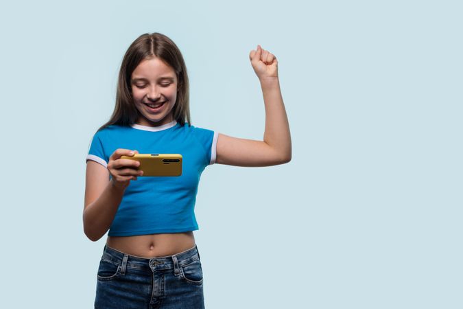 Girl happily cheering while using smartphone, celebrating success