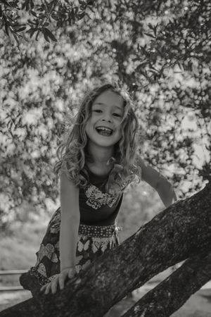 Smiling girl climbing tree in sunny day