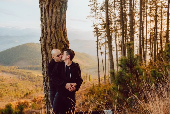 Smiling men hugging near tree in forest on hill