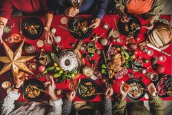 Group of people at festive red table with cake, roast chicken, decorations