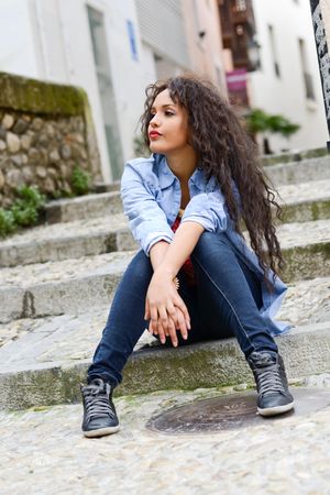 Confident female with curly hair sitting on cement stairs outside