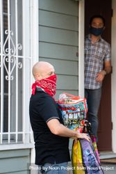 Man delivering bags of groceries to a man waiting at his front door 47m860
