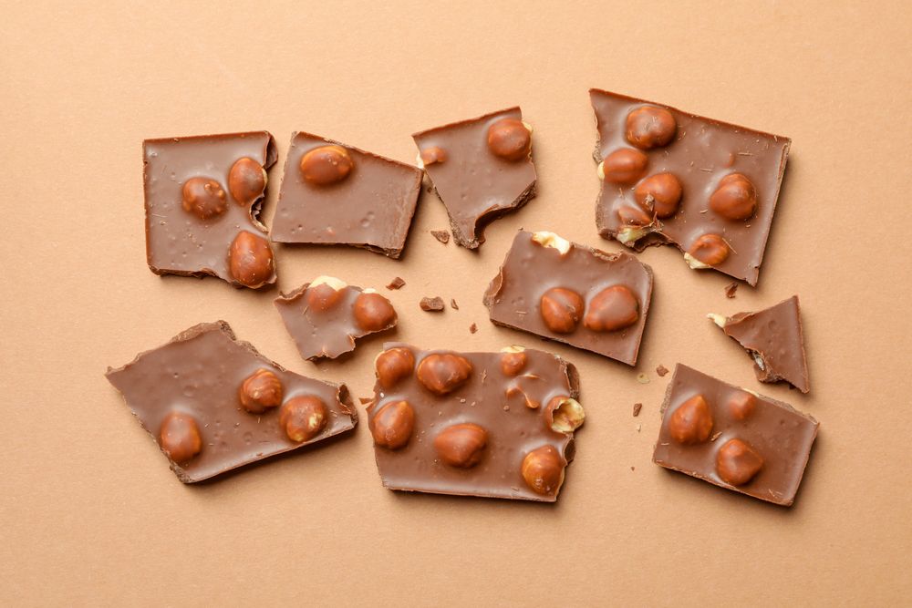 Chocolate pieces on beige background, top view. Sweet food