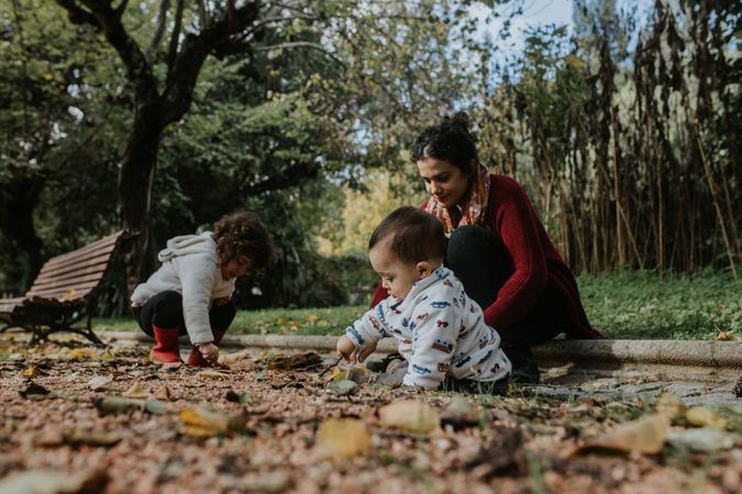 Mother sitting with her two young children playing in the fall leaves