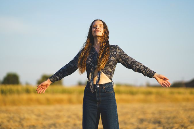 A Joyful Woman Embracing Nature with Outstretched Arms in a Beautiful Sunny Field