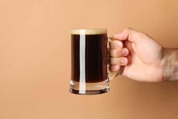 Male hand hold glass of beer on brown background