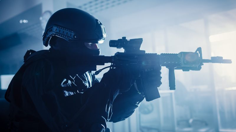 Close Up Portrait of Masked Squad Member of Armed SWAT Police Officers Who Storm a Dark Seized Office Building with Desks and Computers