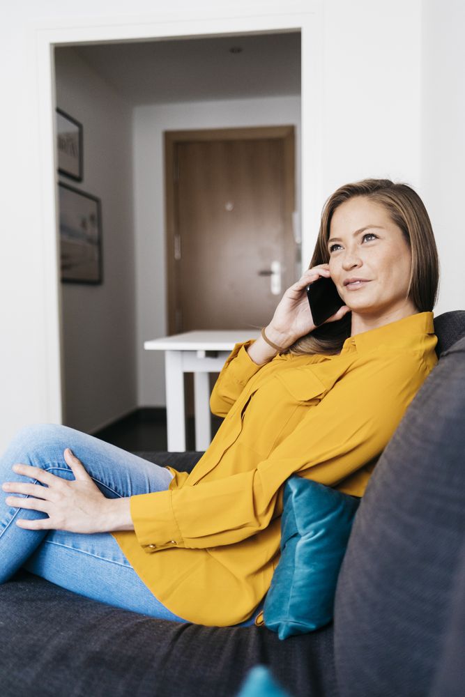 Beautiful adult female sitting on sofa while chatting on smartphone