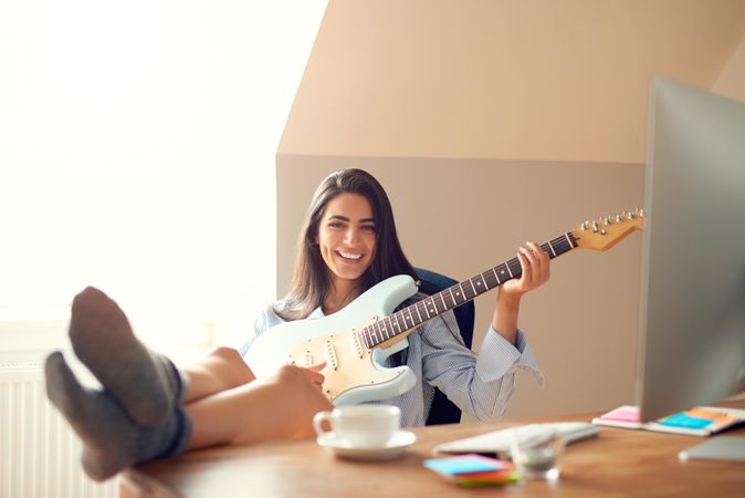 Woman having fun playing guitar at her office desk