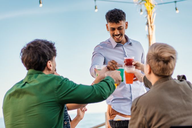 Multicultural friends toasting with colorful drinks at beachside celebration