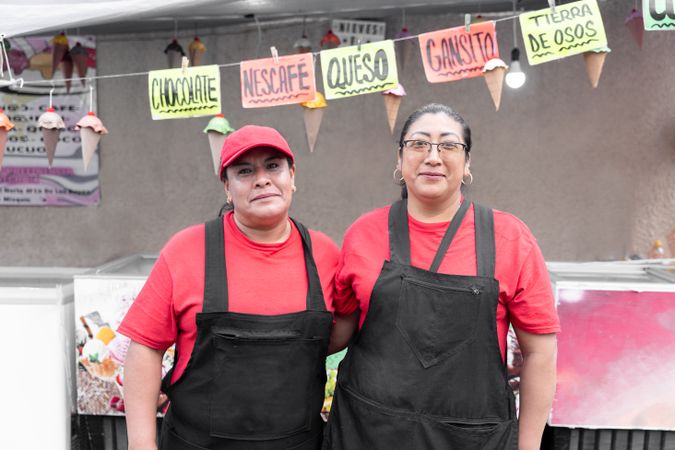 Portrait of two Hispanic adult women posing in front of their ice cream market stall