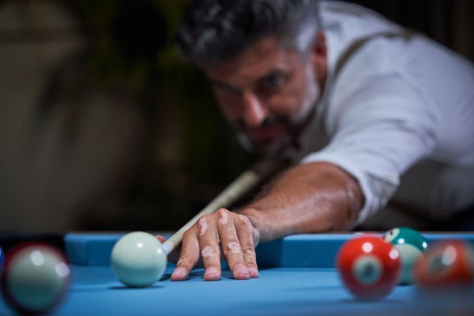 Mature male leaning on pool table and striking ball